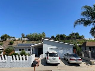 Two cars are parked in front of a house with solar panels on the roof.