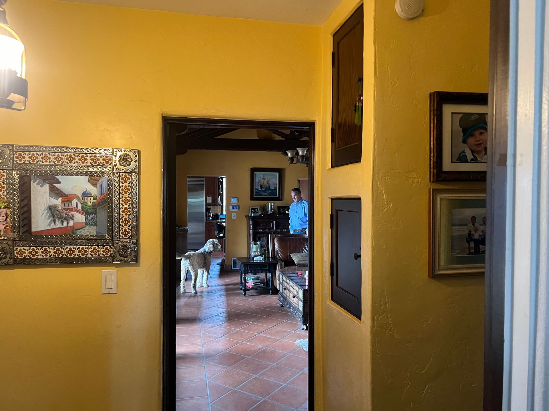 A hallway with yellow walls and pictures on the wall leading to a living room.