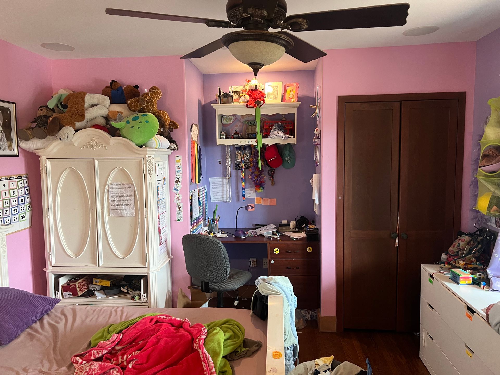 A girl 's bedroom with pink walls and a ceiling fan.