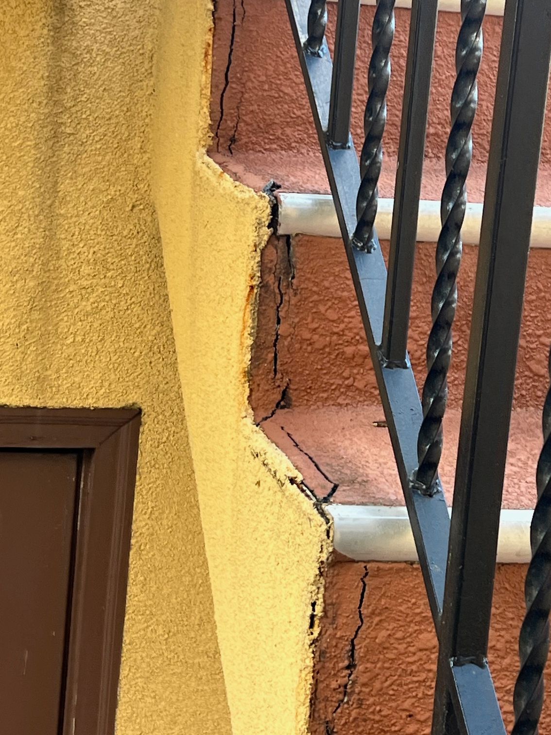 A close up of a cracked wall next to a wrought iron railing.