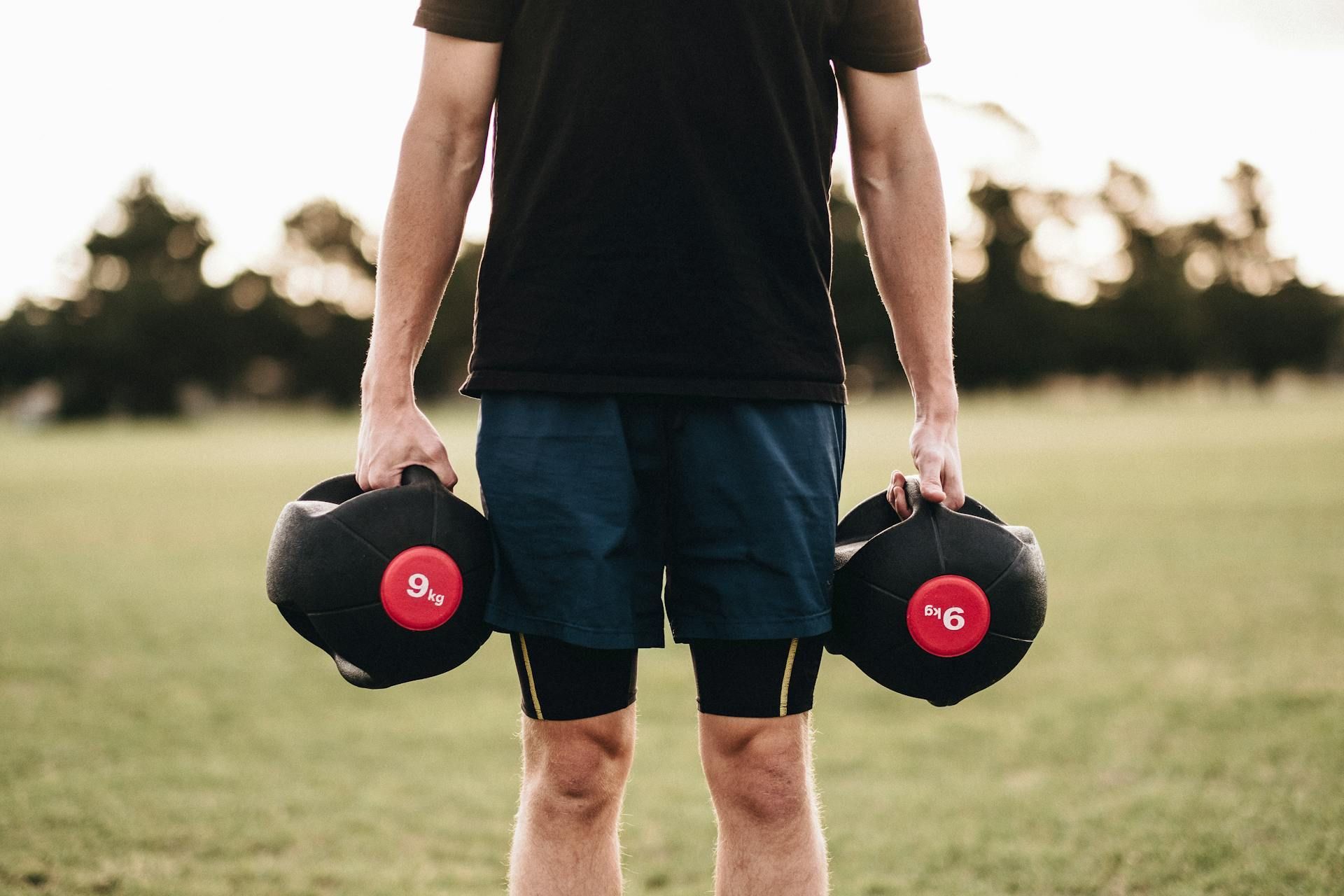 A man is holding two dumbbells in his hands in a field.