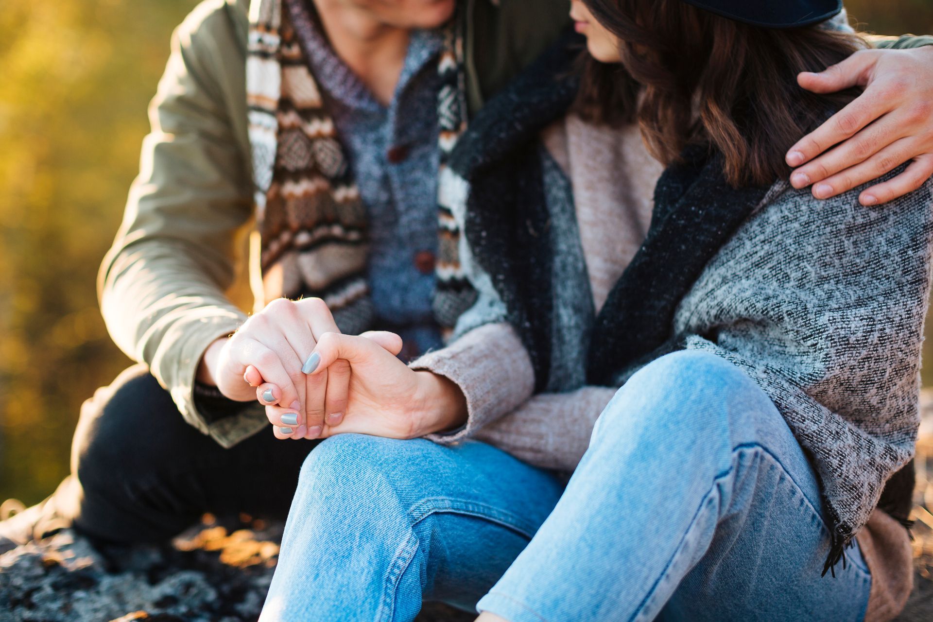 A man and a woman are sitting on a rock holding hands.