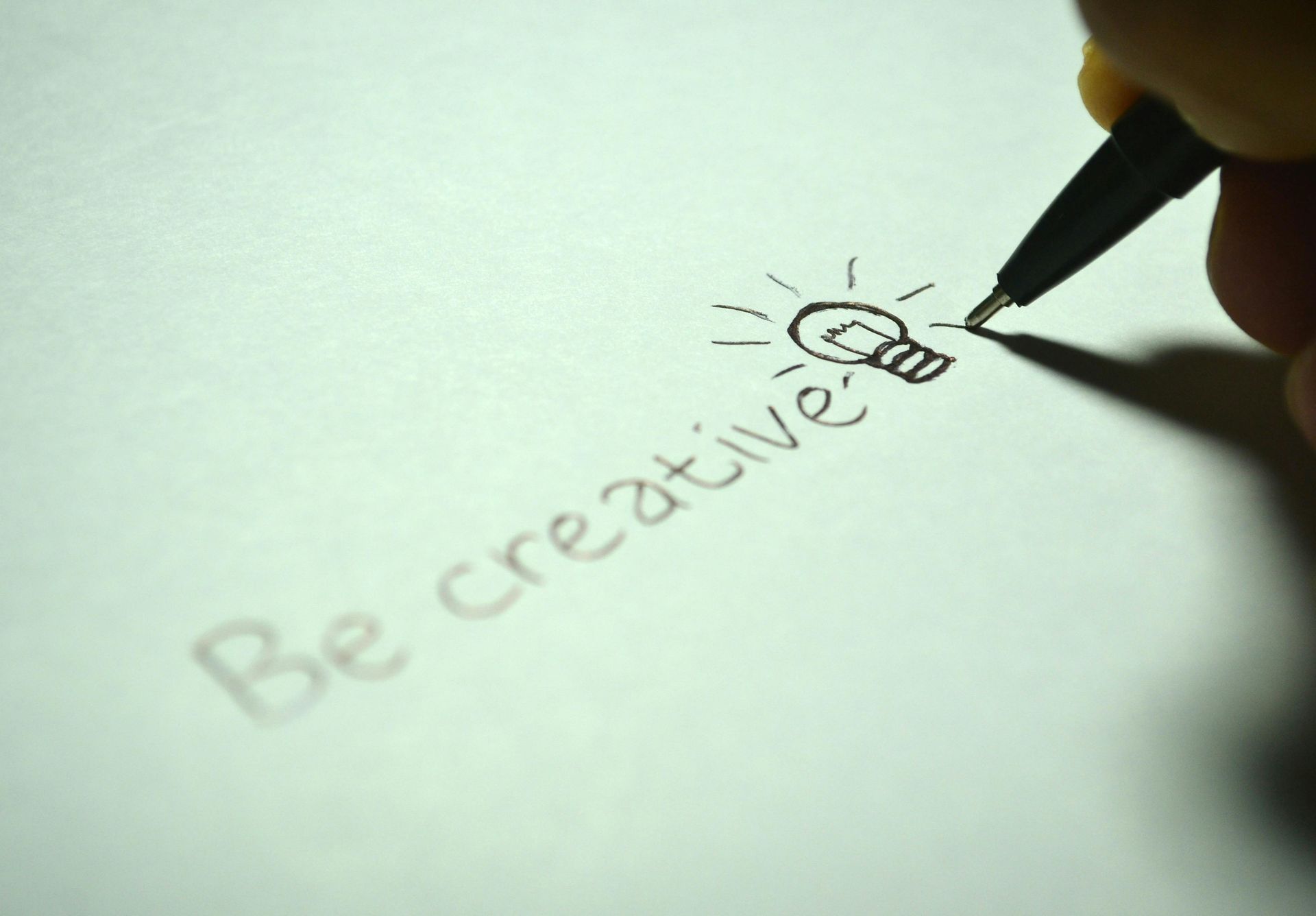 A person is writing the word be creative on a piece of paper