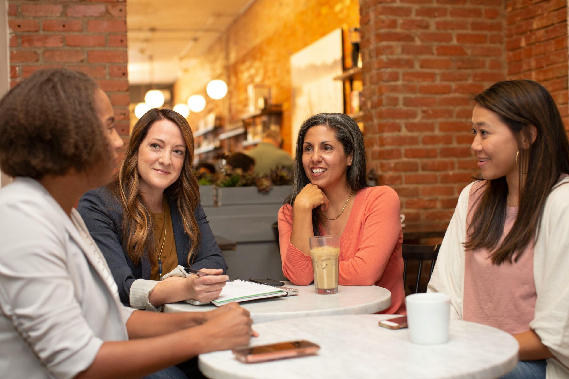 A group of women are sitting at a table in a cafe having a conversation.