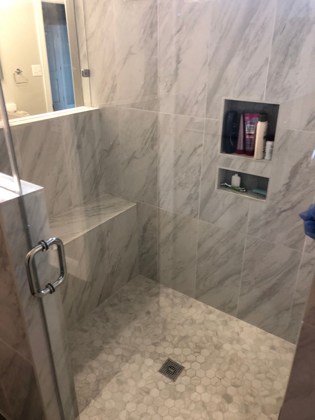 A walk in shower with a glass door and a marble wall.