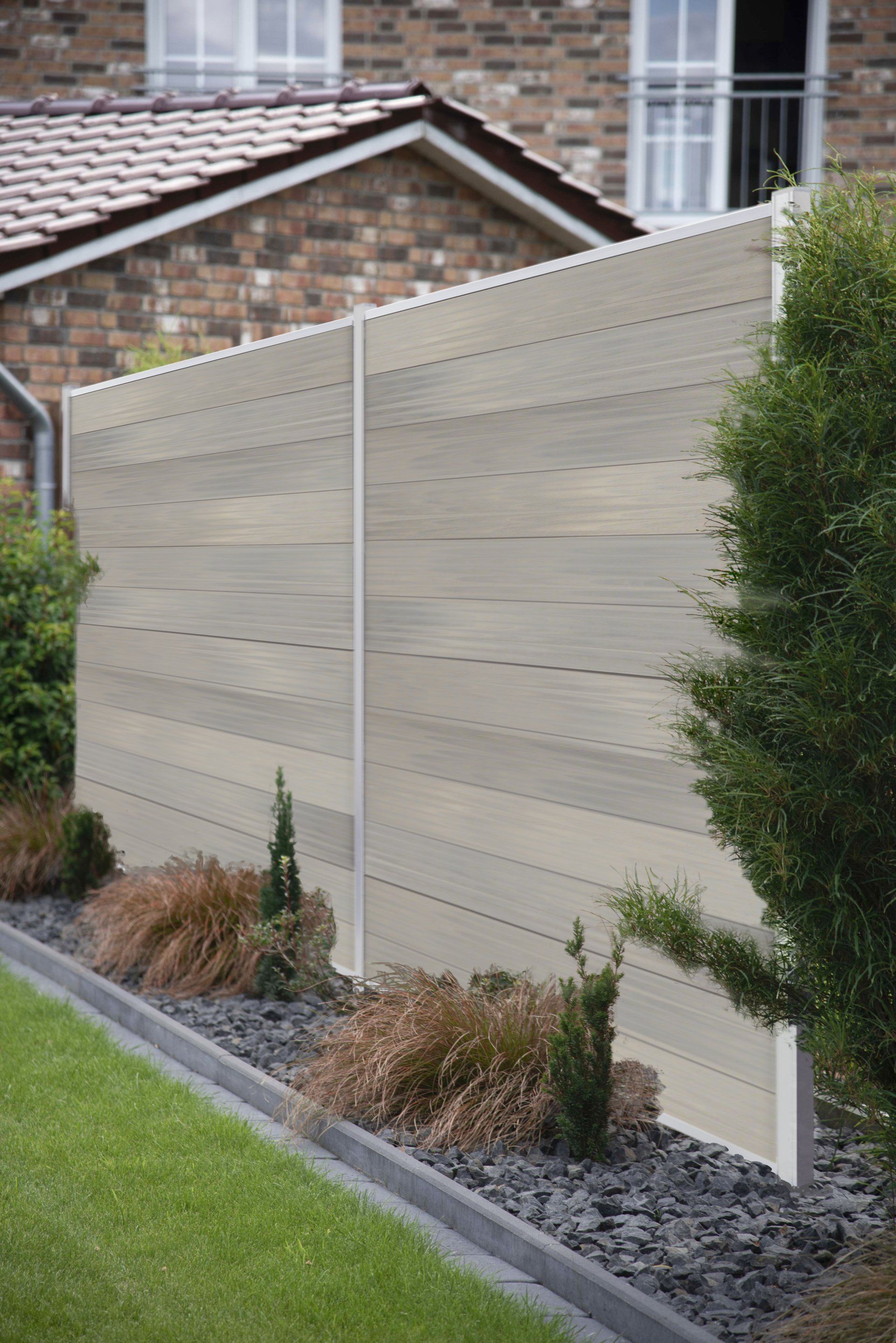 Vor einem Backsteinhaus ist ein weißer Zaun von Pflanzen und Felsen umgeben.