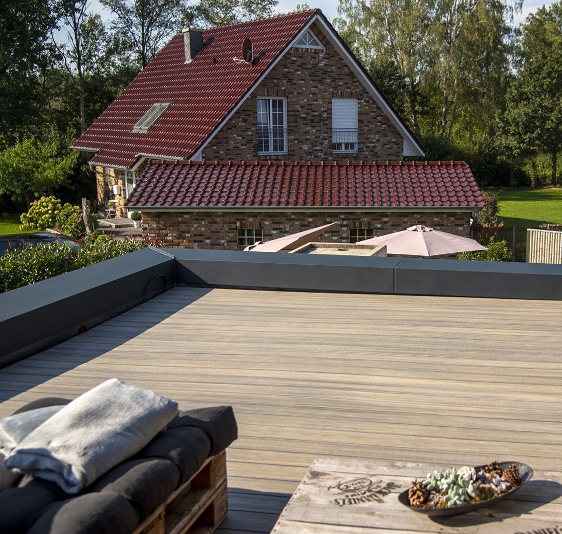 Hinter einer Holzterrasse befindet sich ein Backsteinhaus mit einem roten Ziegeldach