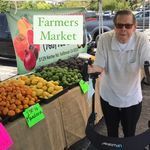A man is standing in front of a fruit stand at a farmers market.