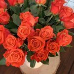 A vase filled with orange roses is sitting on a wooden table.