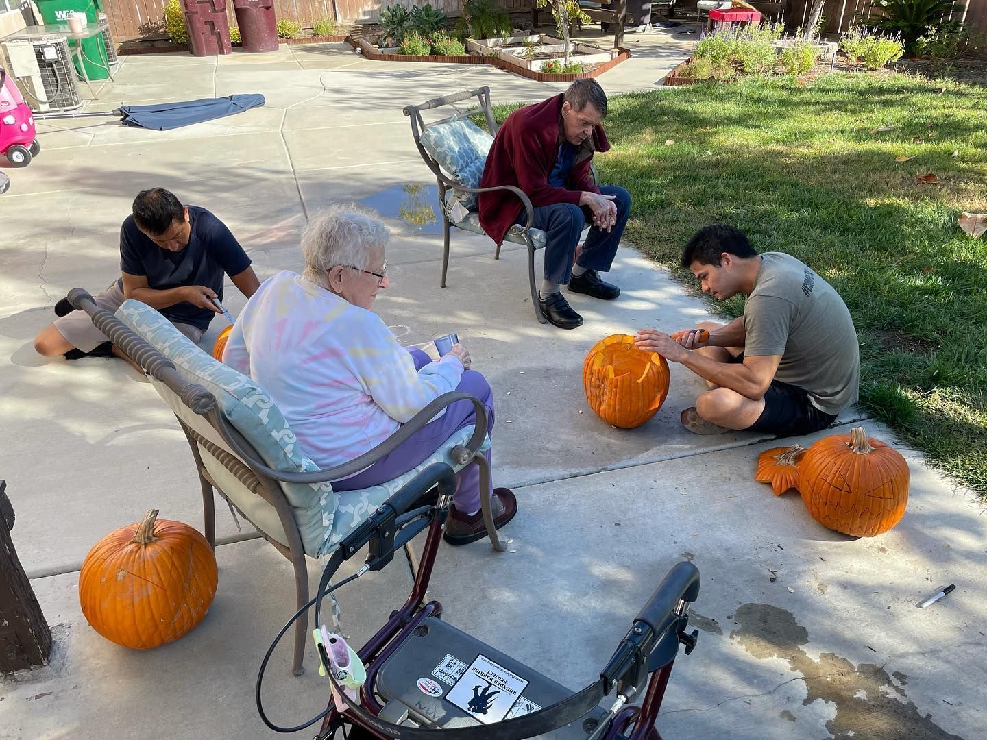A group of people are carving pumpkins in a driveway.