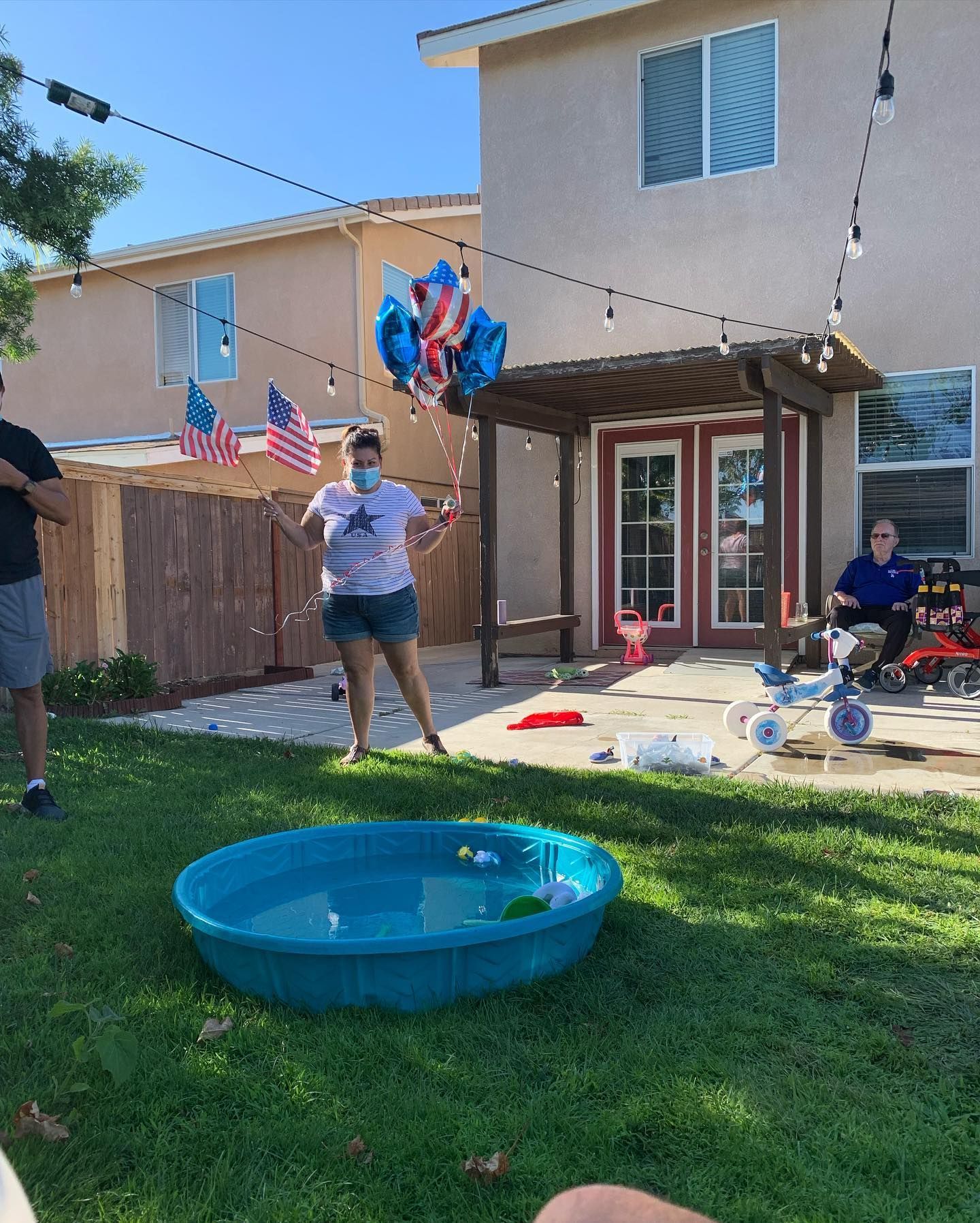 A woman is standing next to a pool in a backyard holding balloons.