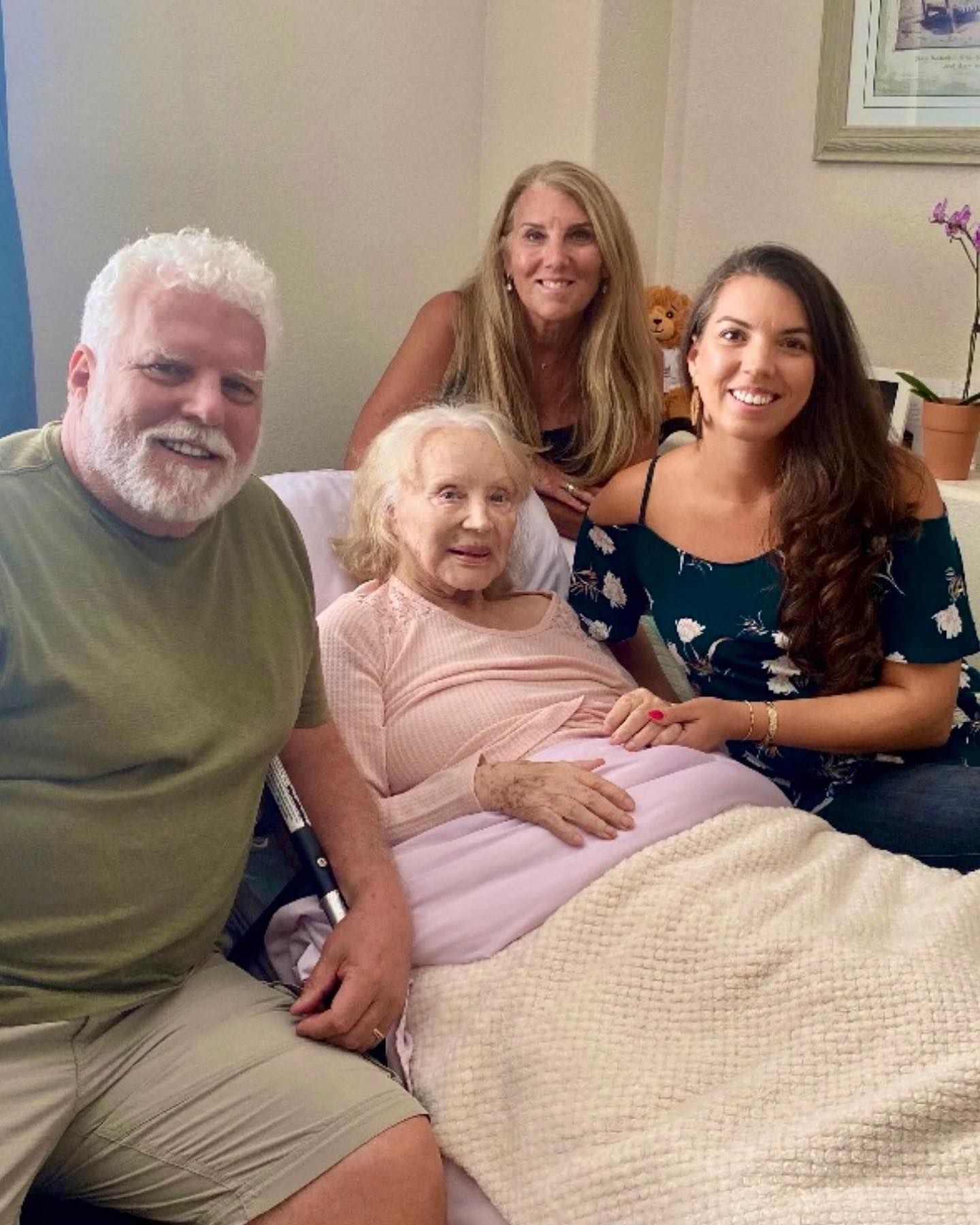 A group of people are posing for a picture with an elderly woman in a hospital bed.