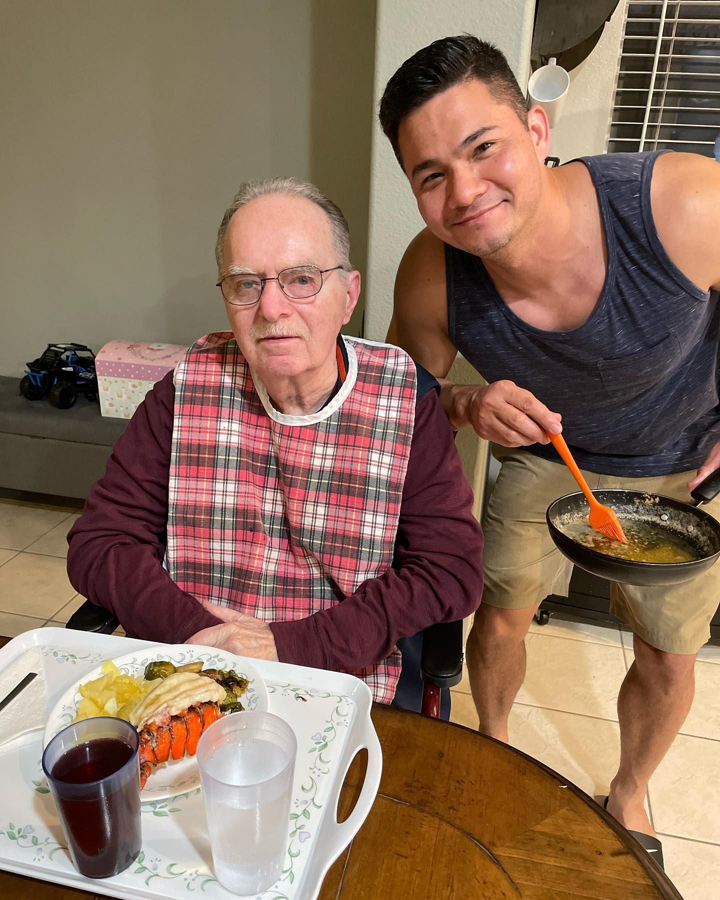 Two men are standing next to each other at a table with a tray of food on it.