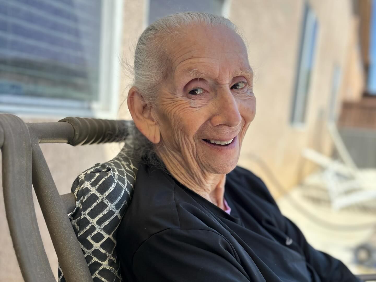 An elderly woman is sitting in a rocking chair and smiling.
