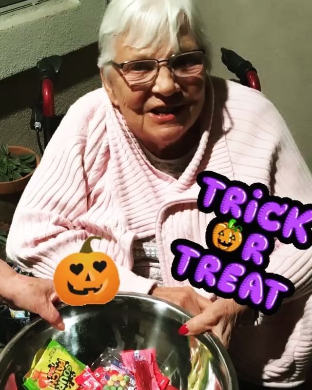 An elderly woman in a wheelchair is holding a bowl of trick or treats