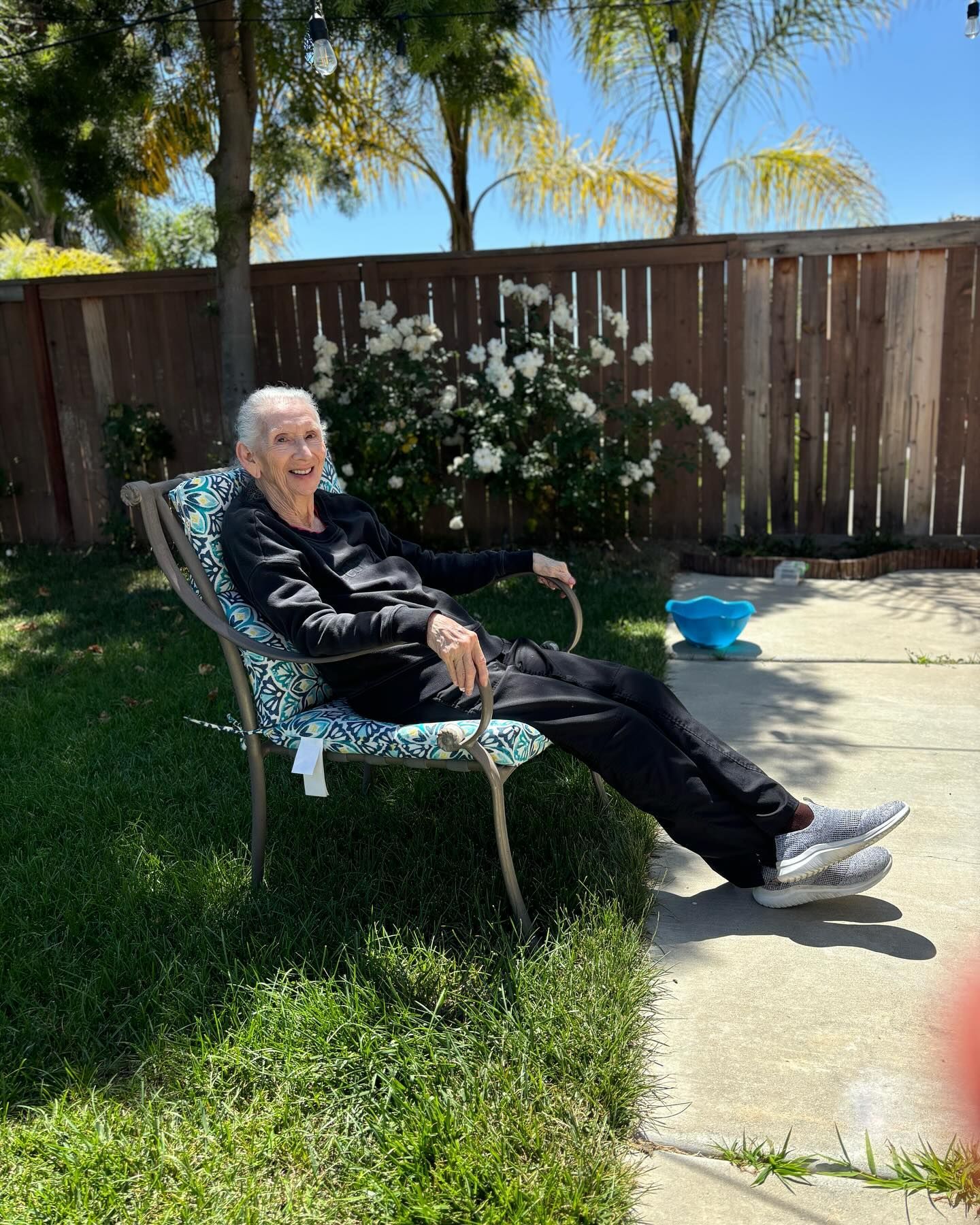 An elderly man is sitting in a chair in a backyard.
