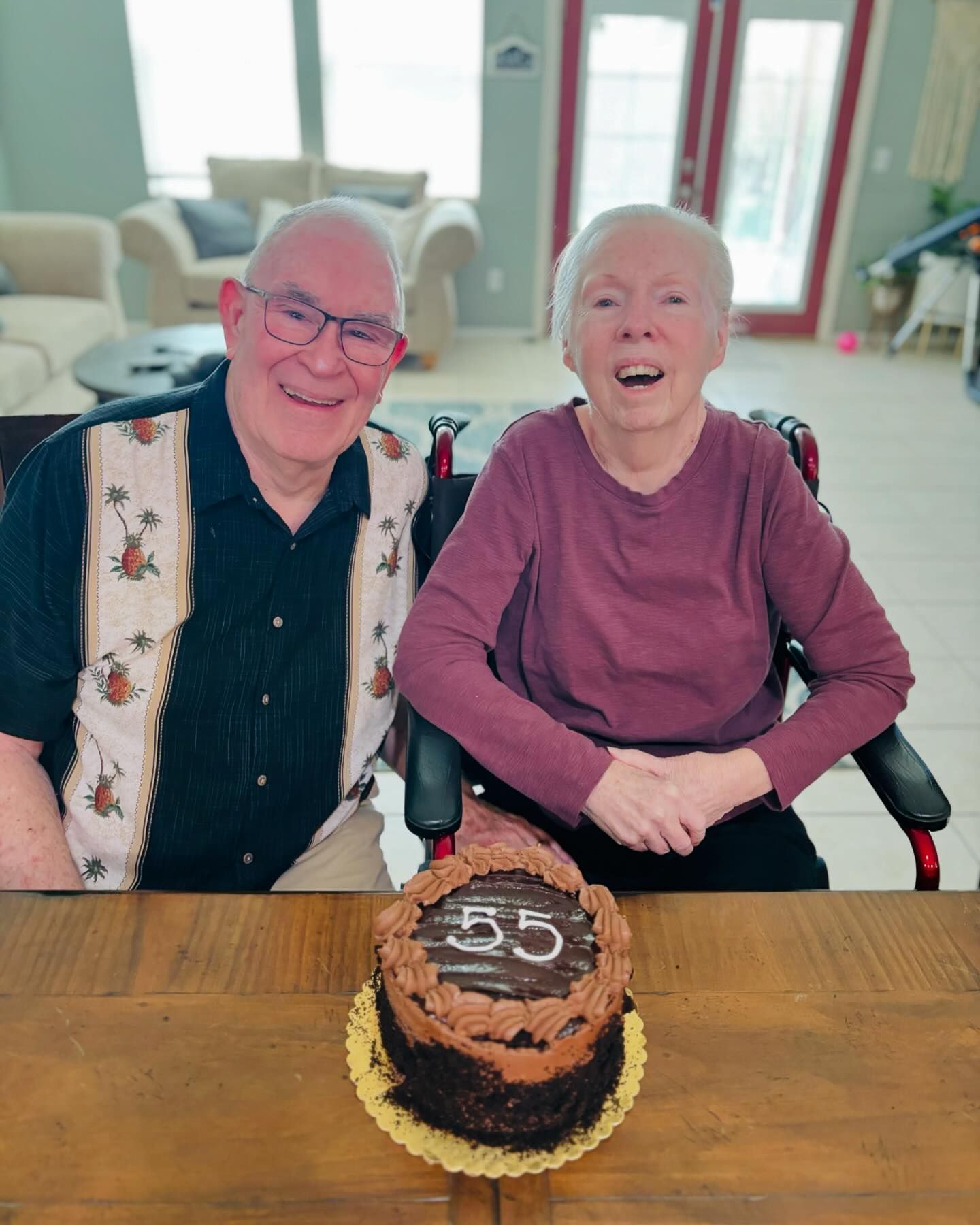A man and a woman are sitting at a table with a cake with the number 55 on it