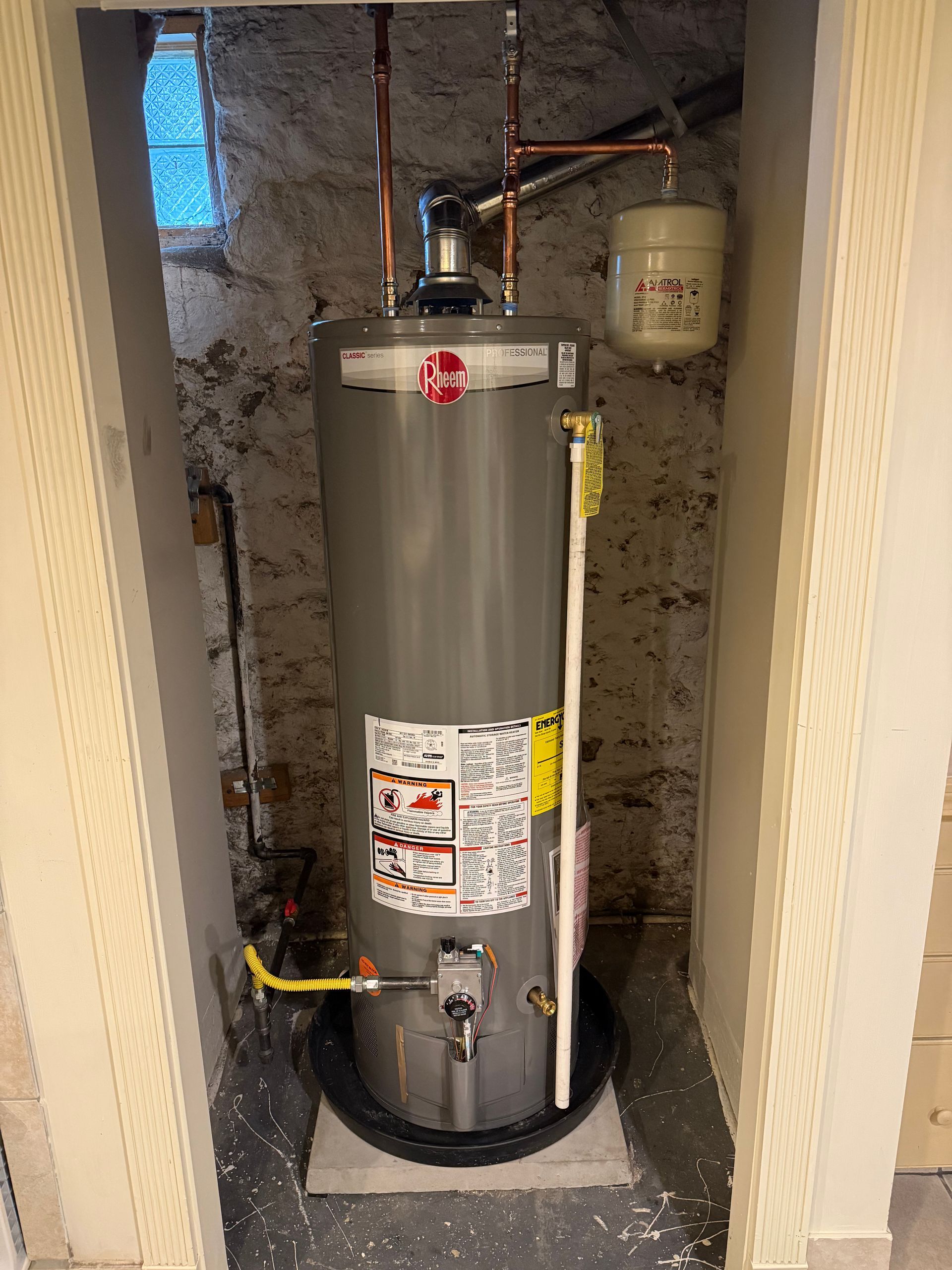 A water heater is sitting in a corner of a room.