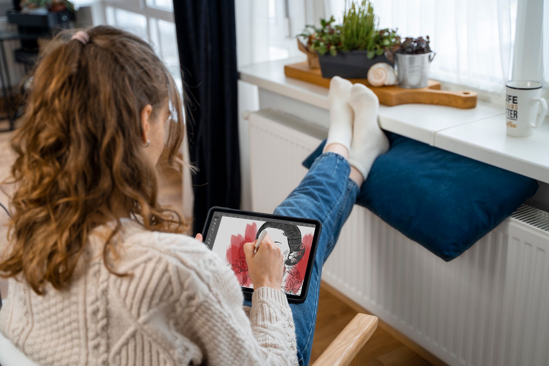 A woman is sitting in a chair with her feet up and using a tablet computer.