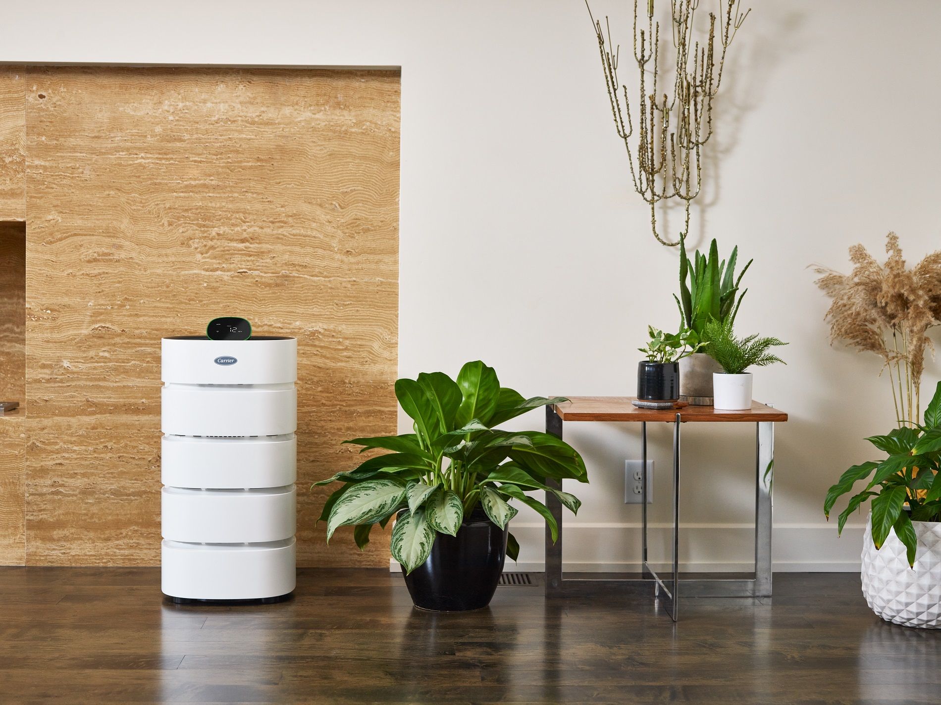 A white air purifier is sitting next to a table with potted plants on it.