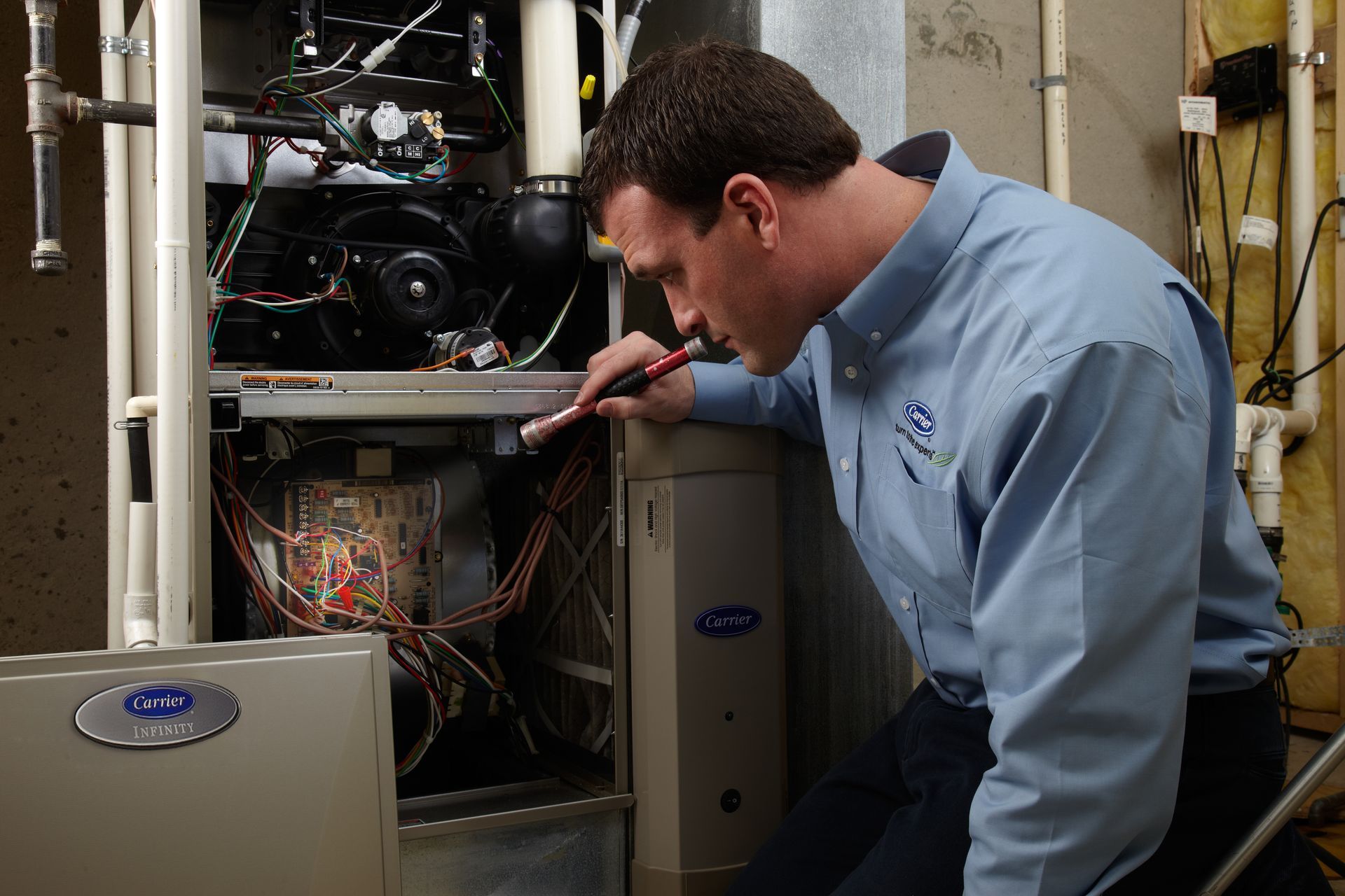 HVAC technician inspecting furnace components with a flashlight in a utility room.