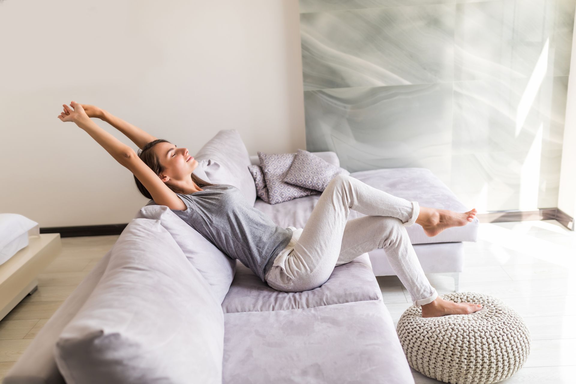Person stretching on a light gray sofa in a bright living room