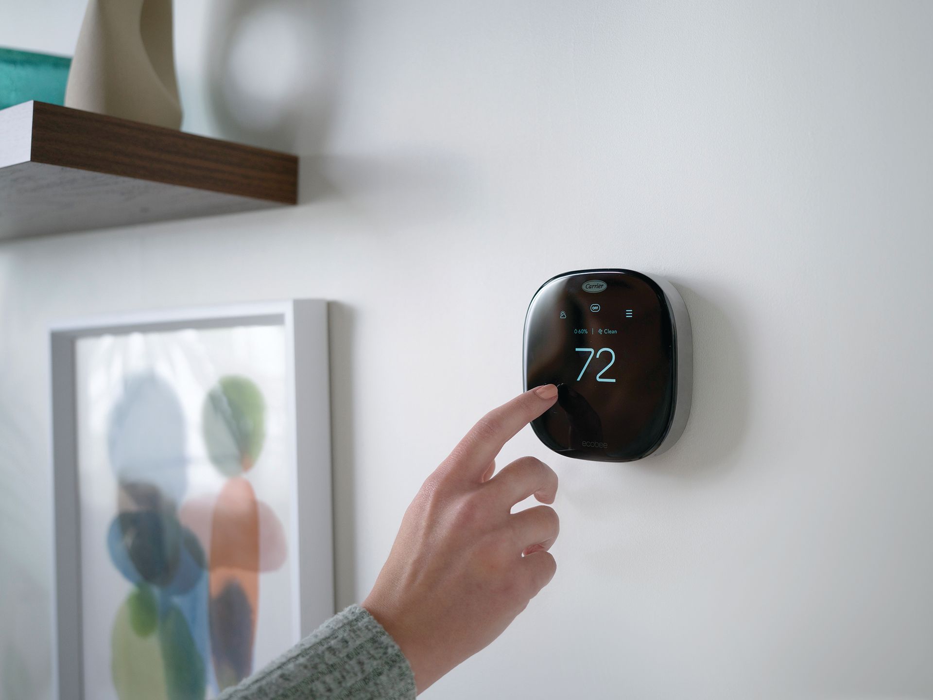 A person is pressing a button on a thermostat on a wall.
