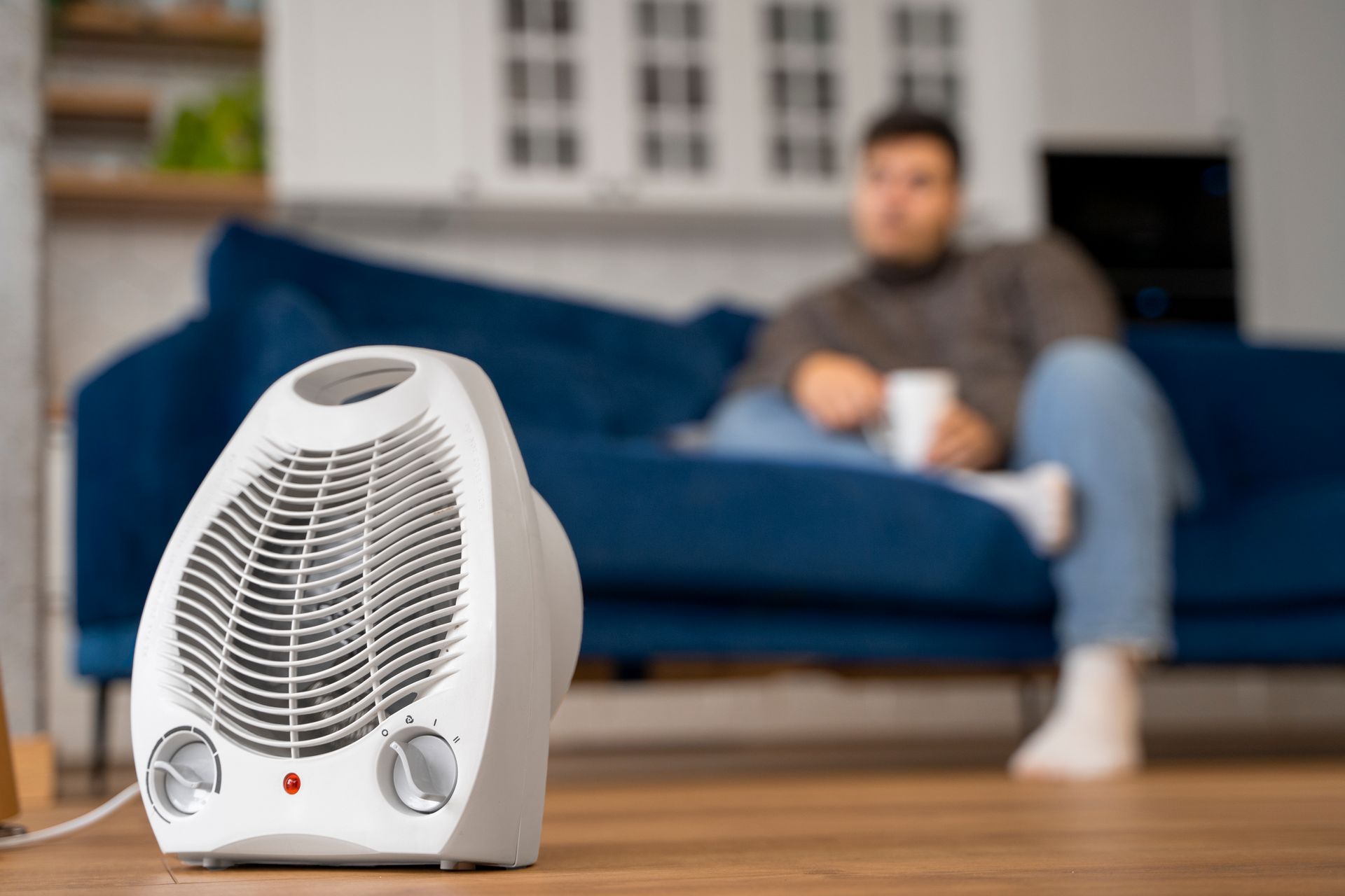 White space heater on a wooden table, with a blurred person sitting on a blue couch in the background