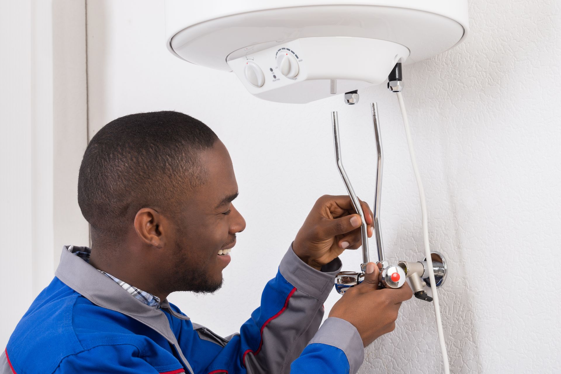 A man is fixing a water heater on a wall.