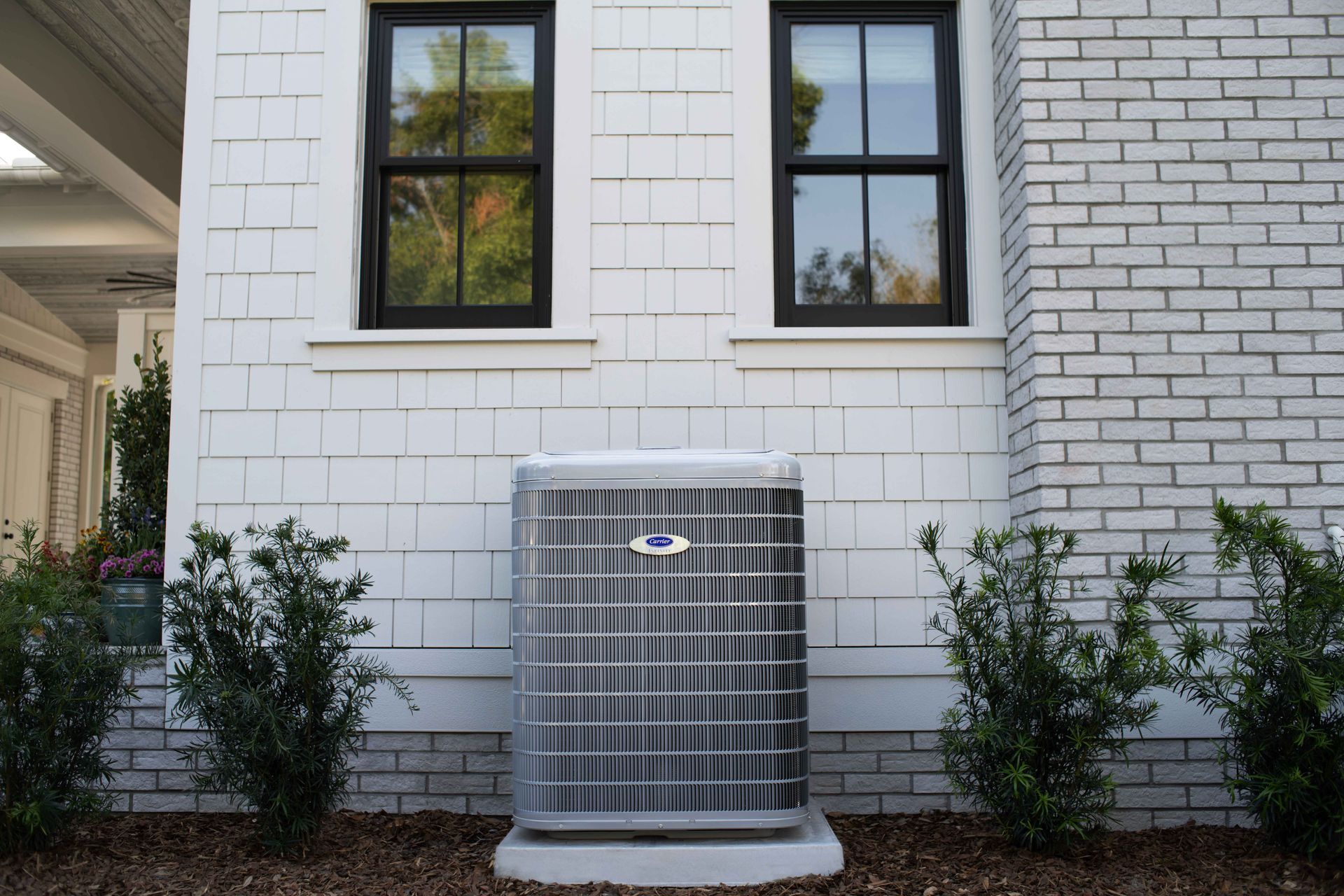 An air conditioner is sitting on the side of a white brick house.