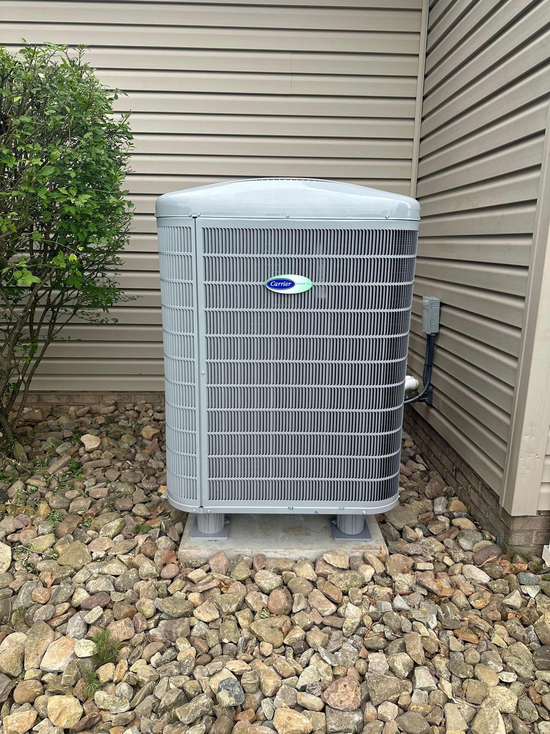 An air conditioner is sitting on top of a pile of rocks next to a house.