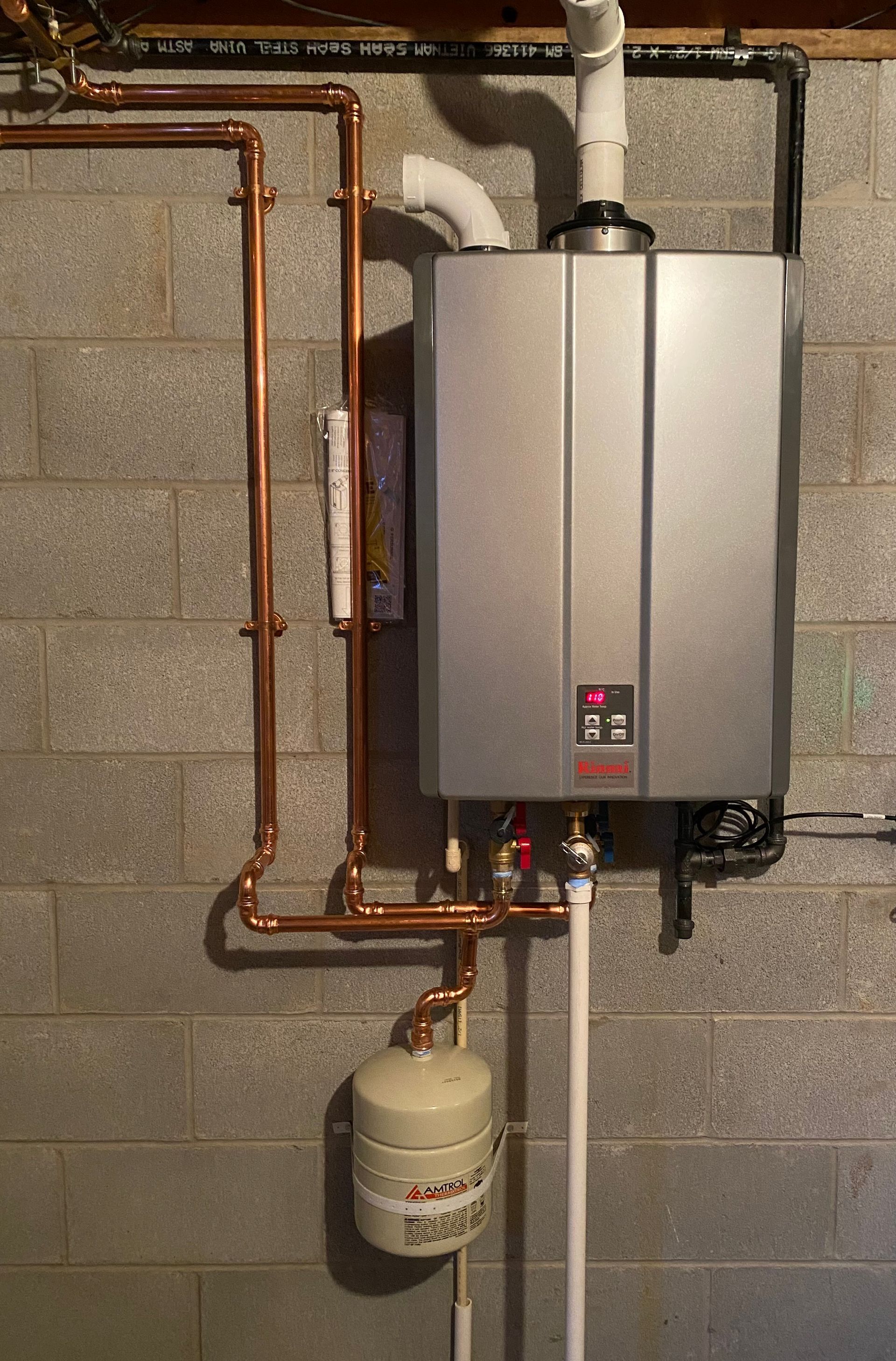 A water heater is hanging on a brick wall next to copper pipes.