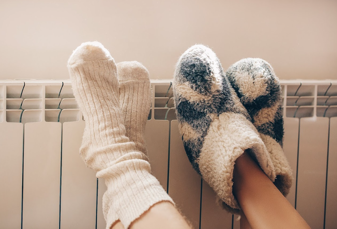 Feet in cozy socks and slippers resting on a radiator, indoors.