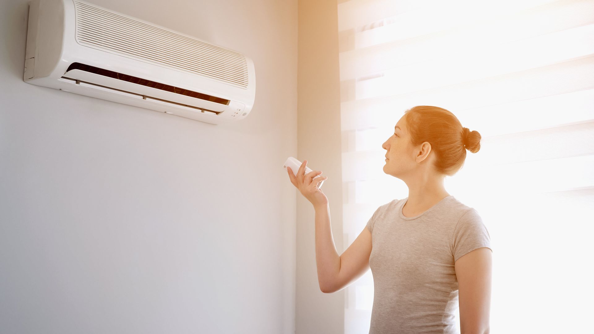 A woman is adjusting her air conditioner in a room.