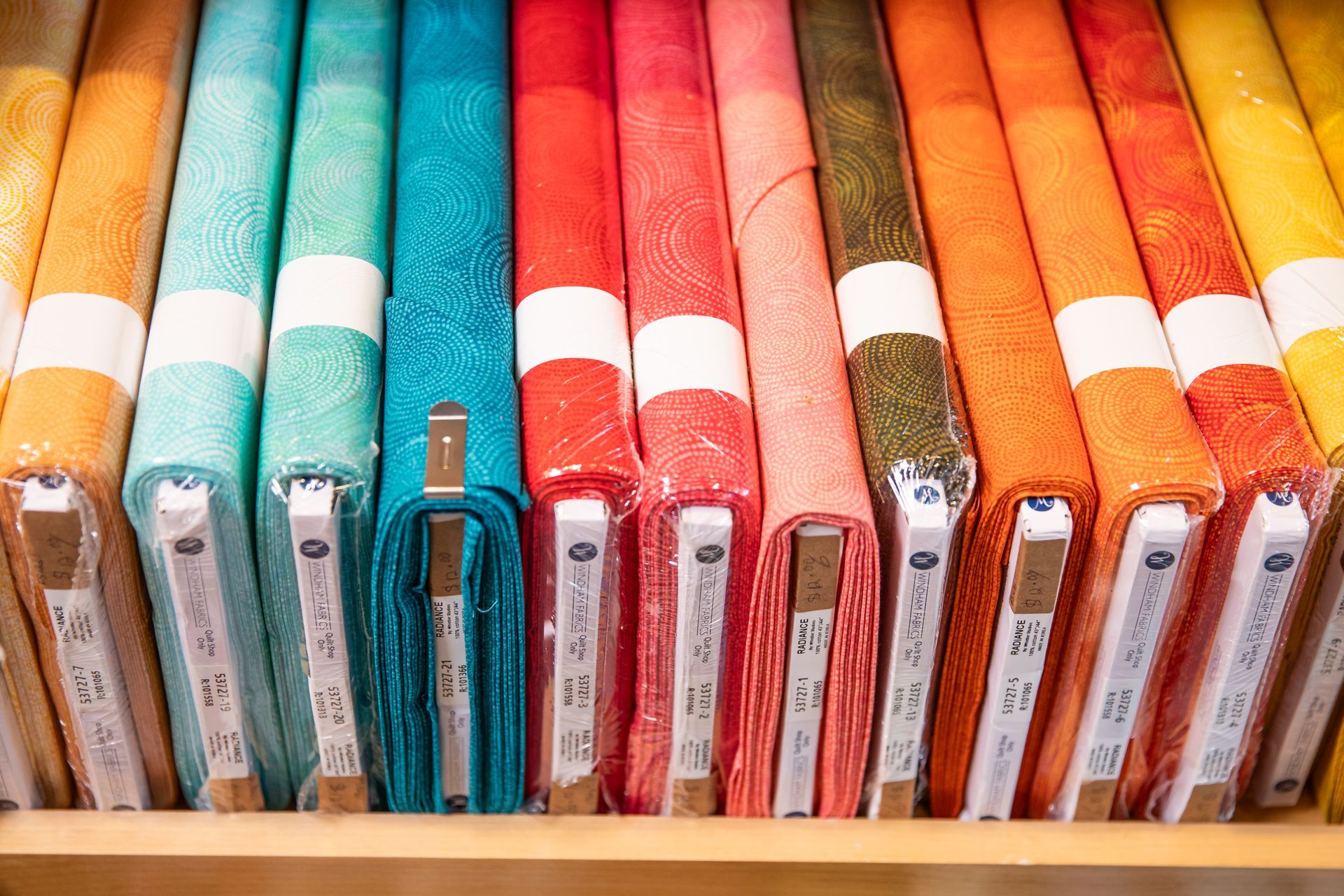 A shelf filled with rolls of fabric of different colors.
