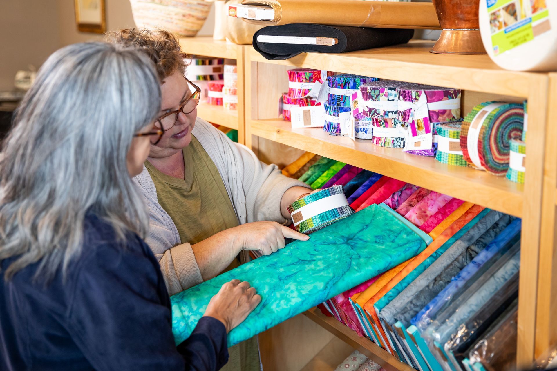 Two women are looking at fabric on a shelf in a store.