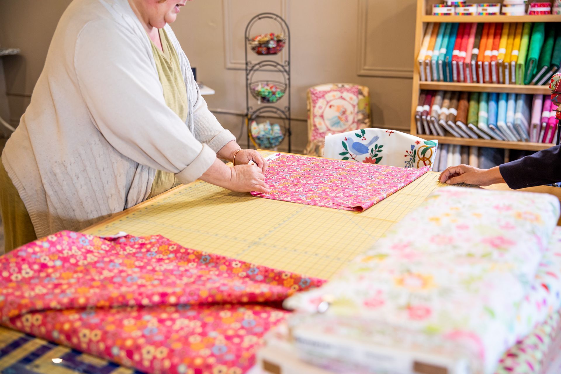 Two women are sitting at a table cutting fabric.
