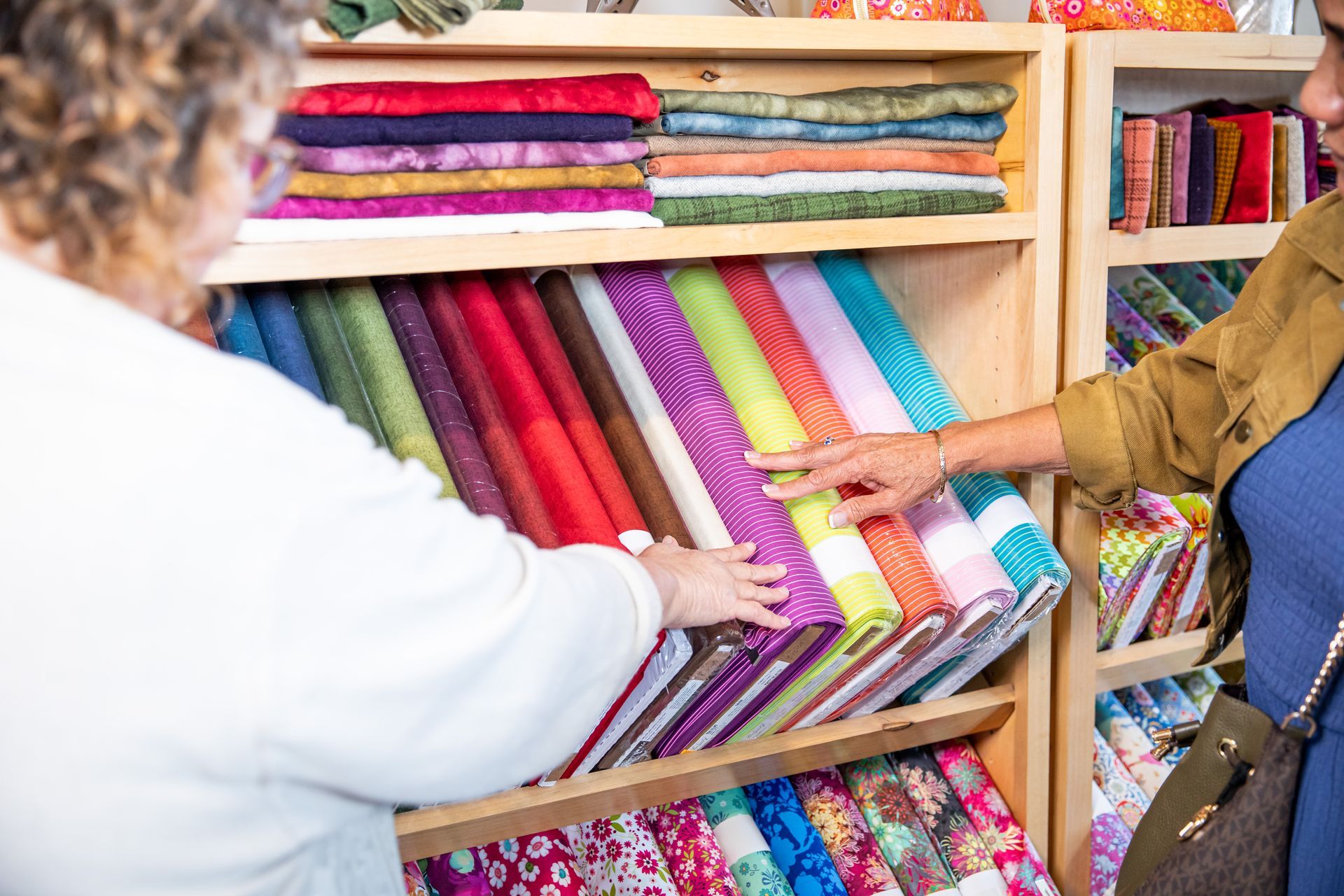 Two women are shopping for fabric in a store.