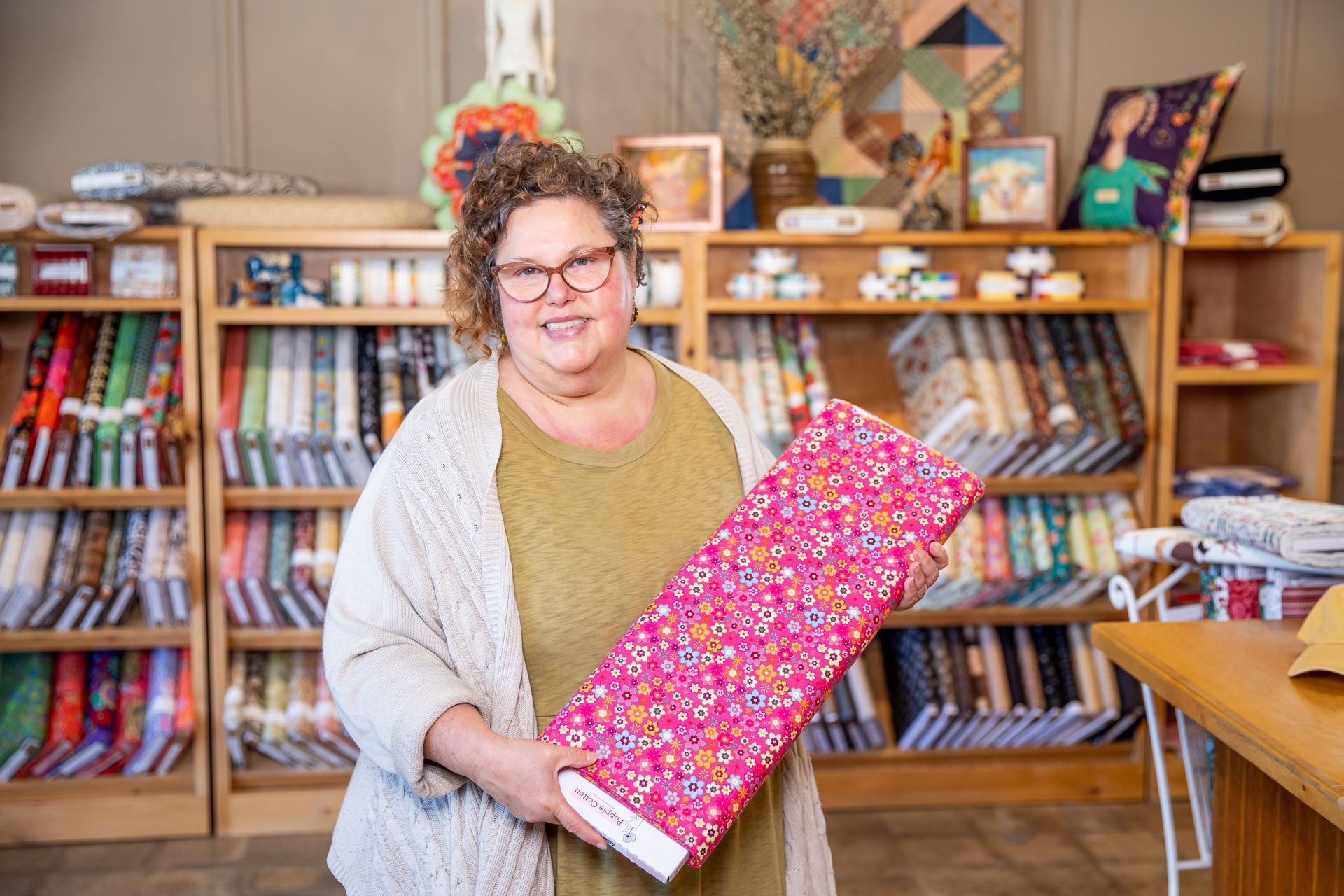 A woman is holding a piece of pink fabric in a sewing shop.