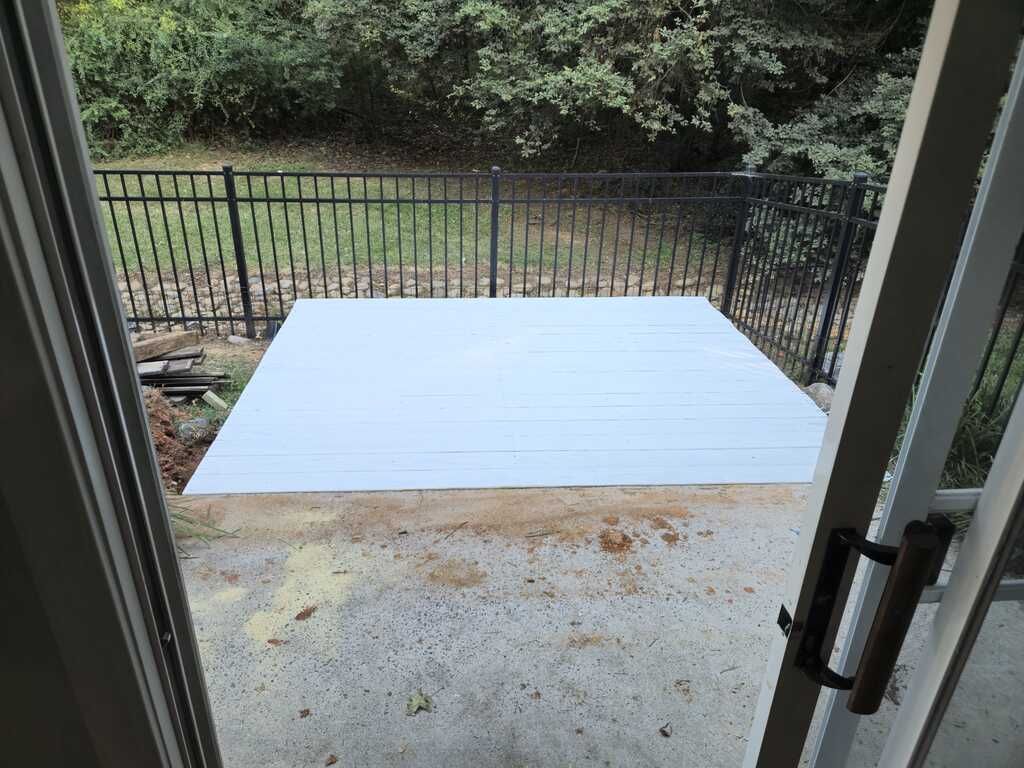 A white deck is sitting on top of a concrete patio next to a fence.