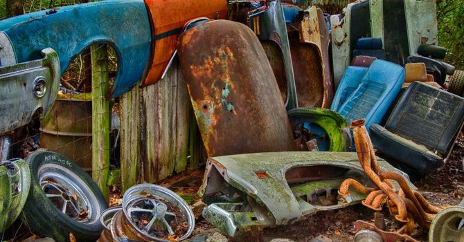 A pile of rusty car parts and tires are sitting on the ground.