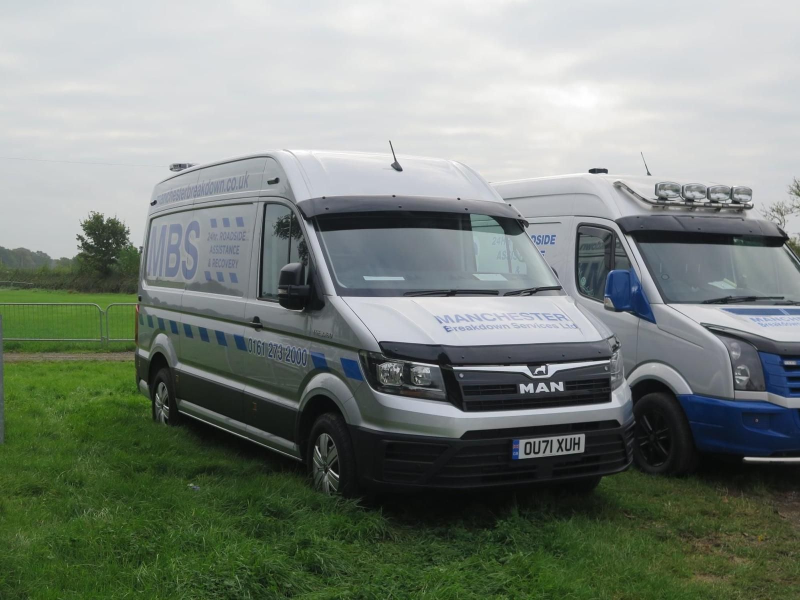 A roadside assistance worker helping a driver with their car, with a service van nearby.
