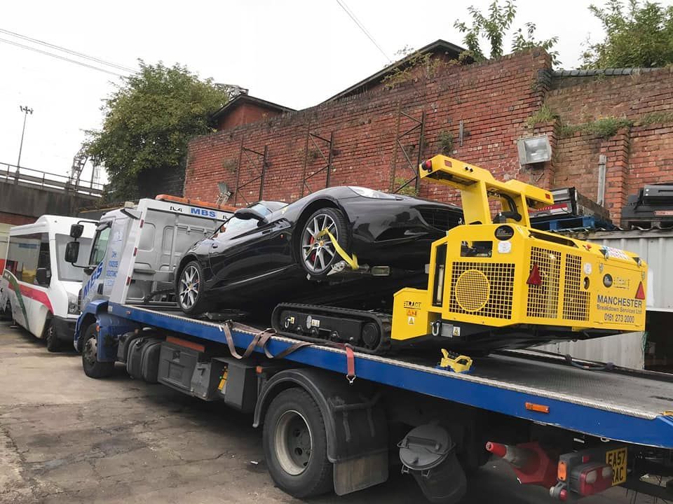 Black sports car being towed on a flatbed truck with a yellow recovery crane.