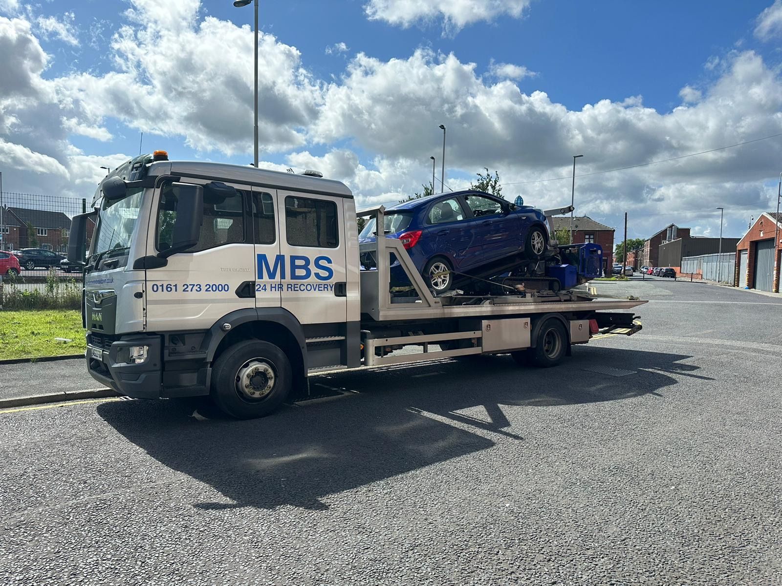 Blue, damaged car on a tow truck on the highway.