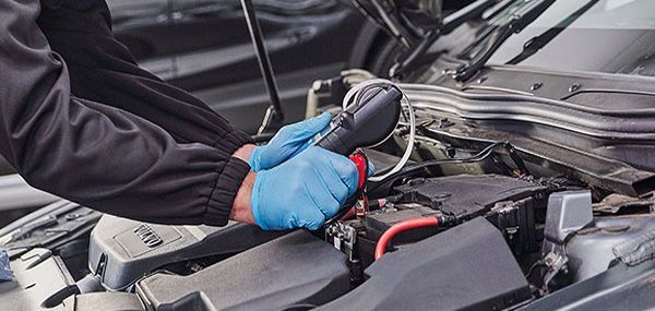 Mechanic in blue gloves using a tool on a car engine.