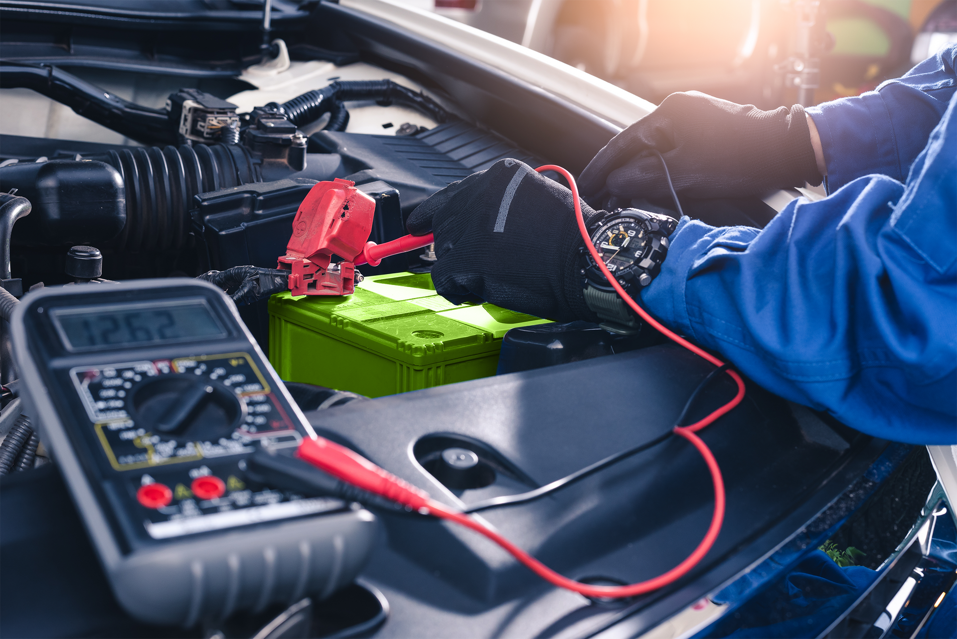 Mechanic testing a car battery with a multimeter in an engine bay.