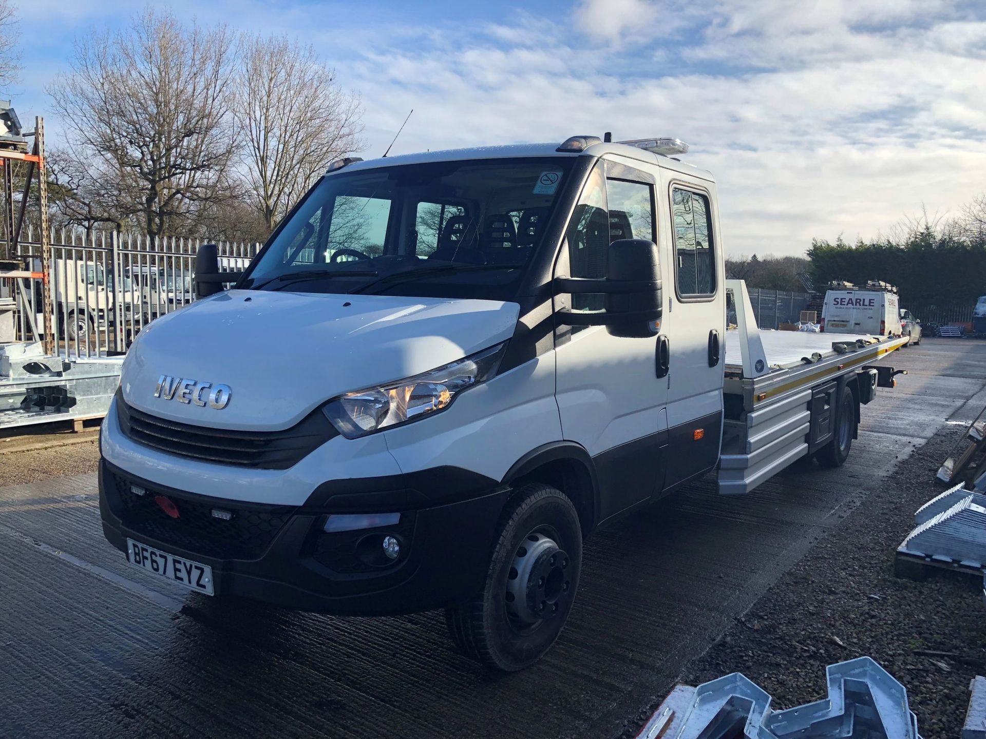 A blue damaged car being towed on a flatbed truck on a highway.