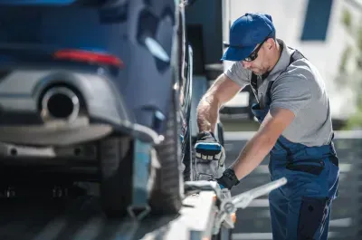 A tow truck driver secures a blue car on a flatbed tow truck.
