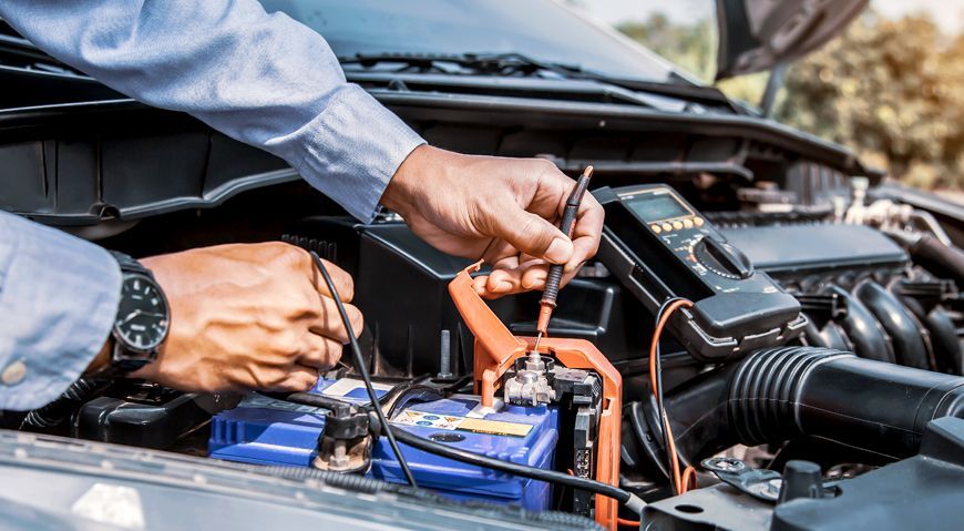 Mechanic testing a car battery with a multimeter in an engine bay.
