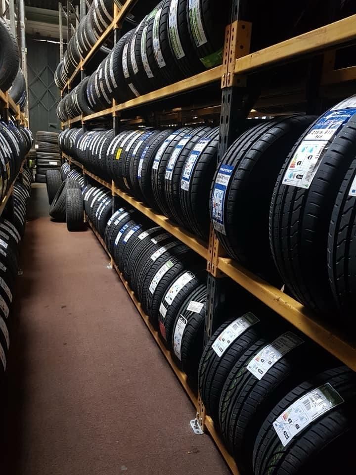 Five new car tires lined up on a road, with a bright sky backdrop.